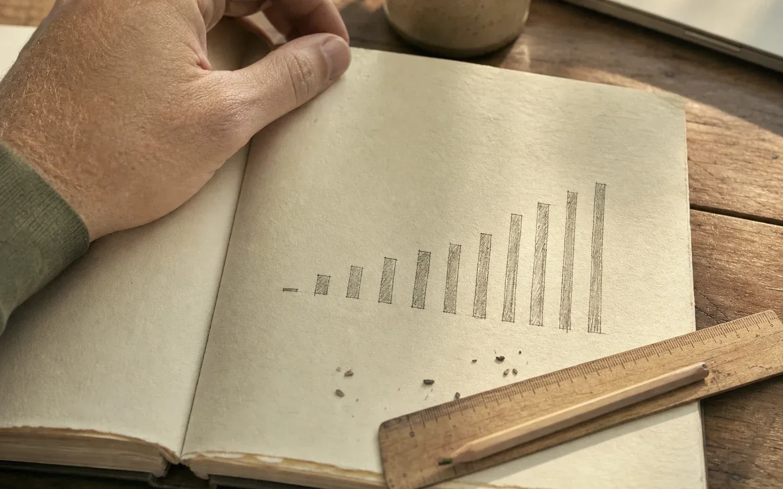 A hand-drawn pencil bar chart in a paper notebook, the first bar barely a mark and the later ones tall, with a wooden ruler and eraser crumbs. AI-generated.